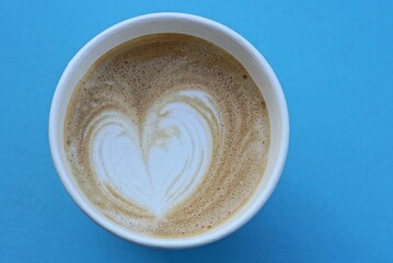 one glass with a brown cappuccino with a white heart in foam stands on a blue table