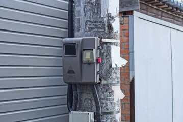 Fototapeta na wymiar one gray electric meter hangs on a concrete pole in the street against the wall