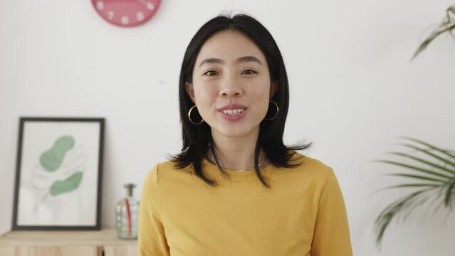 POV - point of view camera footage of young asian woman having an online video call talking to the camera in the living room at home. Portrait of cheerful chinese girl during chat video conference