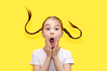 A child girl with an amazed and shocked look and pigtails thrown up in the top on a yellow...
