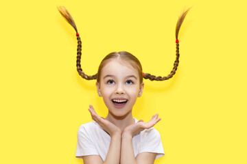 Cheerful girl child throws up her pigtails and laughs on a yellow background. A funny girl has fun...