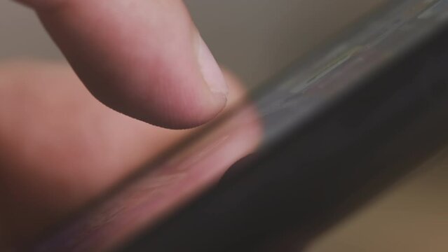 Man looks for necessary app holding modern smartphone. Male finger touches screen of gadget on blurred background extreme close view