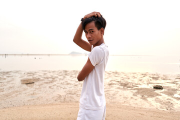 Asian young man posing sensual while looking to the camera next to the sea