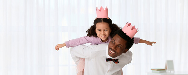 Happy African-American man and his little daughter in paper crowns playing at home