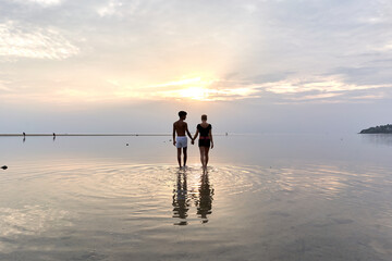 Multiethnic couple holding hands standing in the middle of the sea during sunset