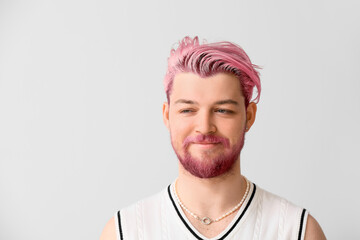 Stylish smiling young man with unusual pink hair and beard on light background