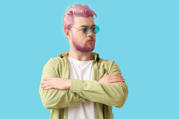 Stylish young man with unusual pink hair and beard on light blue background