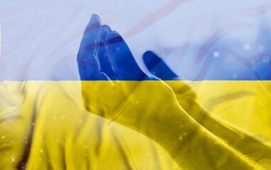 Sad hand with Ukraine flag  double exposition at background praying. Concept of standing with Ukrainian