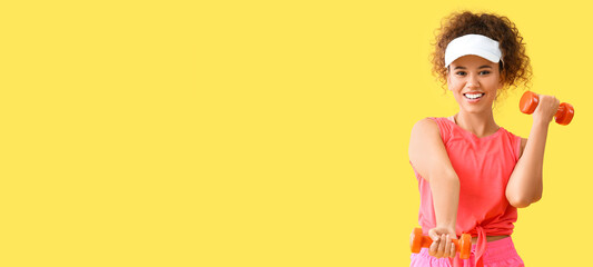 Sporty young African-American woman training with dumbbells on yellow background with space for text