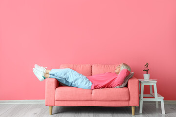 Mature woman relaxing on sofa near pink wall - obrazy, fototapety, plakaty