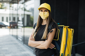Food delivery, portrait of courier caucasian woman wearing facial protective mask, working during covid-19 pandemic with yellow backpack. Quick service, work concept for foreigners, simple profession.