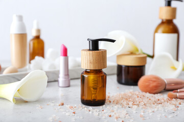 Bottle of essential oil and sea salt on light background