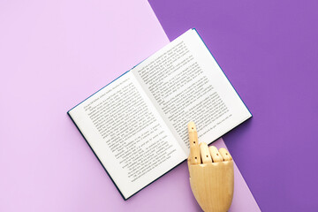 Wooden hand and open book on color background