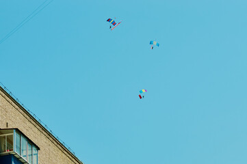 A group of parachutists in a clear sky with colored bright parachutes. Roof of a residential building with a balcony. The flag of Russia and the Soviet Union are developing in the sky.