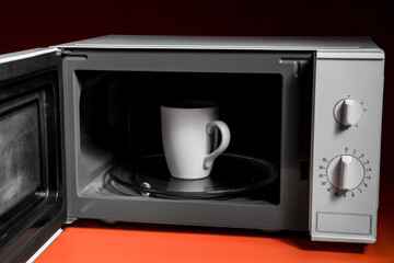 Cup in modern microwave oven on color background