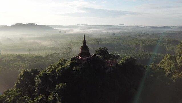 Aerial footage early morning mist gradually Move over a white pagoda atop a hill surrounded by the Asian rain forest.