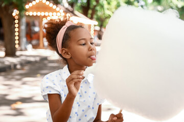 Little African-American girl eating cotton candy outdoors