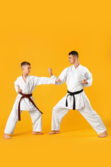 Boy practicing karate with instructor on yellow background
