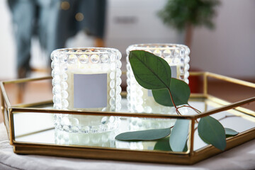 Holders with burning candles and eucalyptus branch on table, closeup