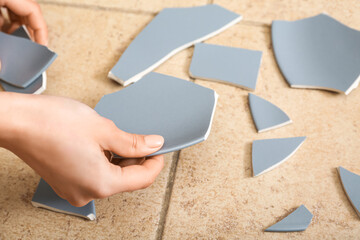 Female hands with broken ceramic plate on color tile, closeup