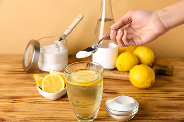 Woman adding baking soda into glass with water on wooden table