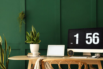 Workplace with modern computer, laptop and houseplants near green wall