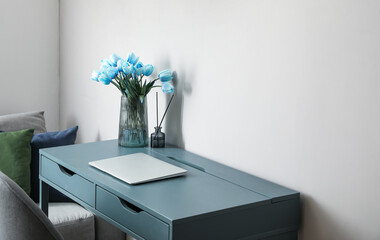 Workplace with laptop, blue tulips in vase and reed diffuser near light wall