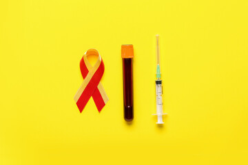 Awareness ribbon with blood sample and syringe on yellow background. Hepatitis concept