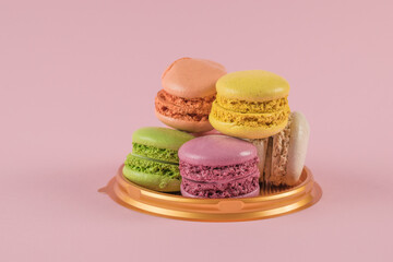 Multicolored macaroon cookies on a plastic stand on a pink background.