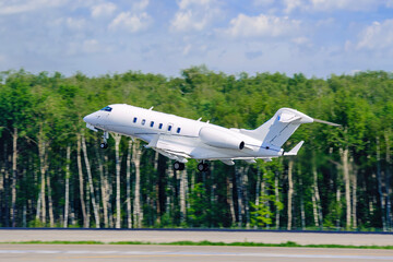 A modern private white business jet takes off against the backdrop of a forest. Jet business...