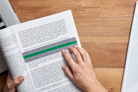 Student with dyslexia reading a book with the help of a coloured reading ruler