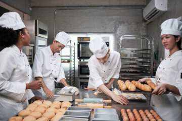 Multiracial professional gourmet team, four chefs in white cook uniforms and aprons knead pastry...