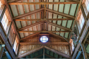 Barn ceiling with crossbeams and corrugated metal roof, circular window.