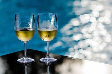 Two glasses of white wine put on table at swimming pool for Holiday and summer drink concept.