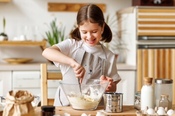 Happy child girl cooking pastry in kitchen