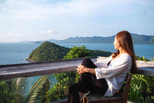 Portrait image of a young asian woman sitting and looking at a beautiful sea view from resort terrace