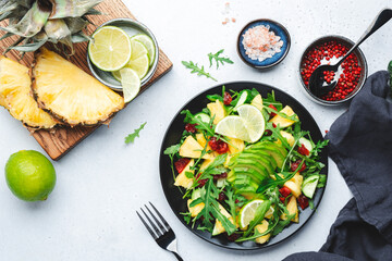 Summer vegan salad with juicy pineapple, fresh arugula, avocado and dried cranberry on white stone kitchen table, top view. Healthy eating, clean diet food, weight loss concept