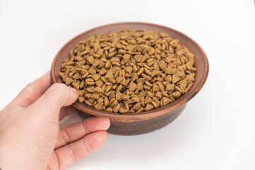 Pet food. A man is holding a brown bowl of dry food in his hand. Pelleted food against a white background. Triangular pellets.