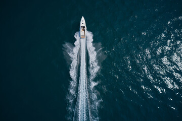 Obraz premium Speed boat faster movement on the water top view. Speedboat movement on the water. Large white boat driving on dark water. Speedboat wave speed water. Speedboat on dark blue water aerial view.