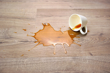 A cup of coffee fell on laminate, coffee spilled on floor.