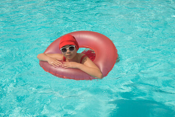 woman with vintage bathing cap and glasses in inflatable red ring in swimming pool in summer