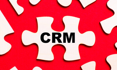 On a bright red background, white puzzles. In one of the pieces of the puzzle, the text CRM Customer Relationship Management