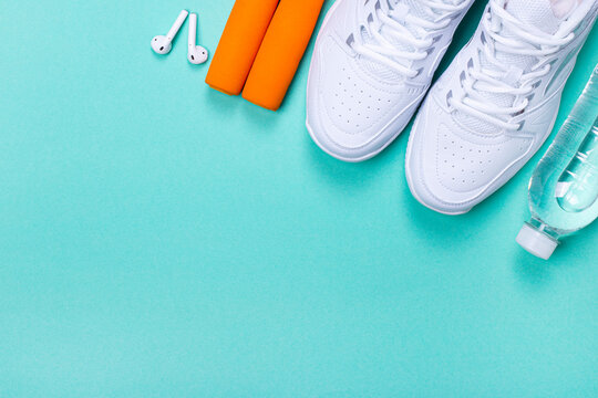 On a light green background, white sneakers, a bottle of water, a jump rope and headphones. The concept of a healthy lifestyle. Copy space
