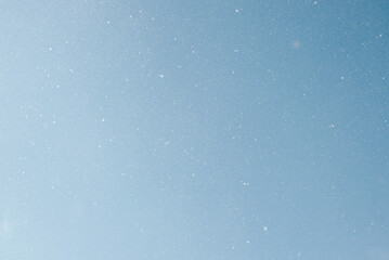 Falling snow, white snowflakes on clear blue sky outdoors. Defocus light slow snowfall in winter