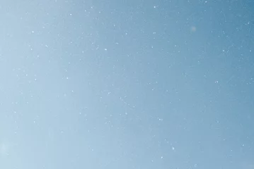 Foto op Plexiglas anti-reflex Falling snow, white snowflakes on clear blue sky outdoors. Defocus light slow snowfall in winter © Sergio