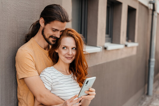 Young couple hugging each other, in front of a brown wall with cell phone