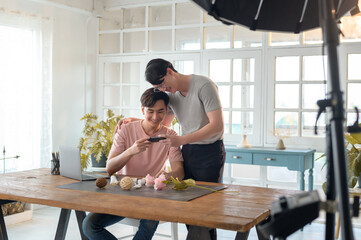 Young smiling gay couple working on new project and shooting pictures of new product by smartphone
