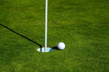 Obraz premium Golf ball on lip of cup on grass background. Golf hole. Golf ball on the lawn. Sport golf background with copy space.