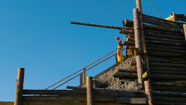 Industrial Gold Mine Workers Descending Down Wooden Stairs. Workers In Hardhats Carrying Equipment For Gold Mining. Mine Workers Preparing For Gold Excavation Process. Excavated Rock Piles. Geology