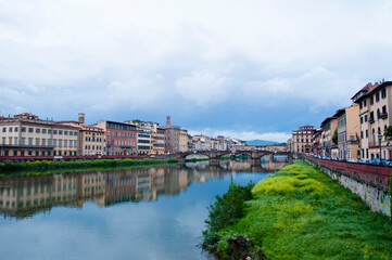 Fototapeta na wymiar Overgrown Arno river bank with Ponte Santa Trinita StTrinity bridge and Florence cityscape in Italy